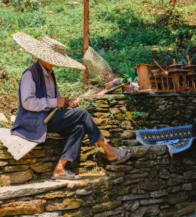 An old craftsman sits on steps in Pokhara while gently beading his bamboo threads to make a sun protector used in the rice and paddy fields